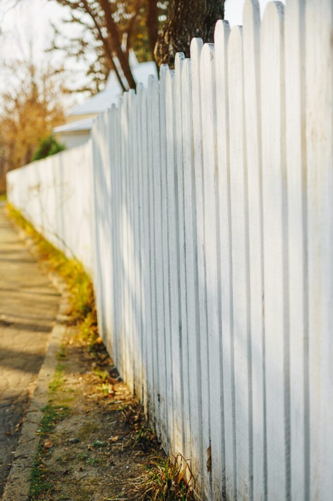 High white fence in front of the house in autumn with shadows from branches.
